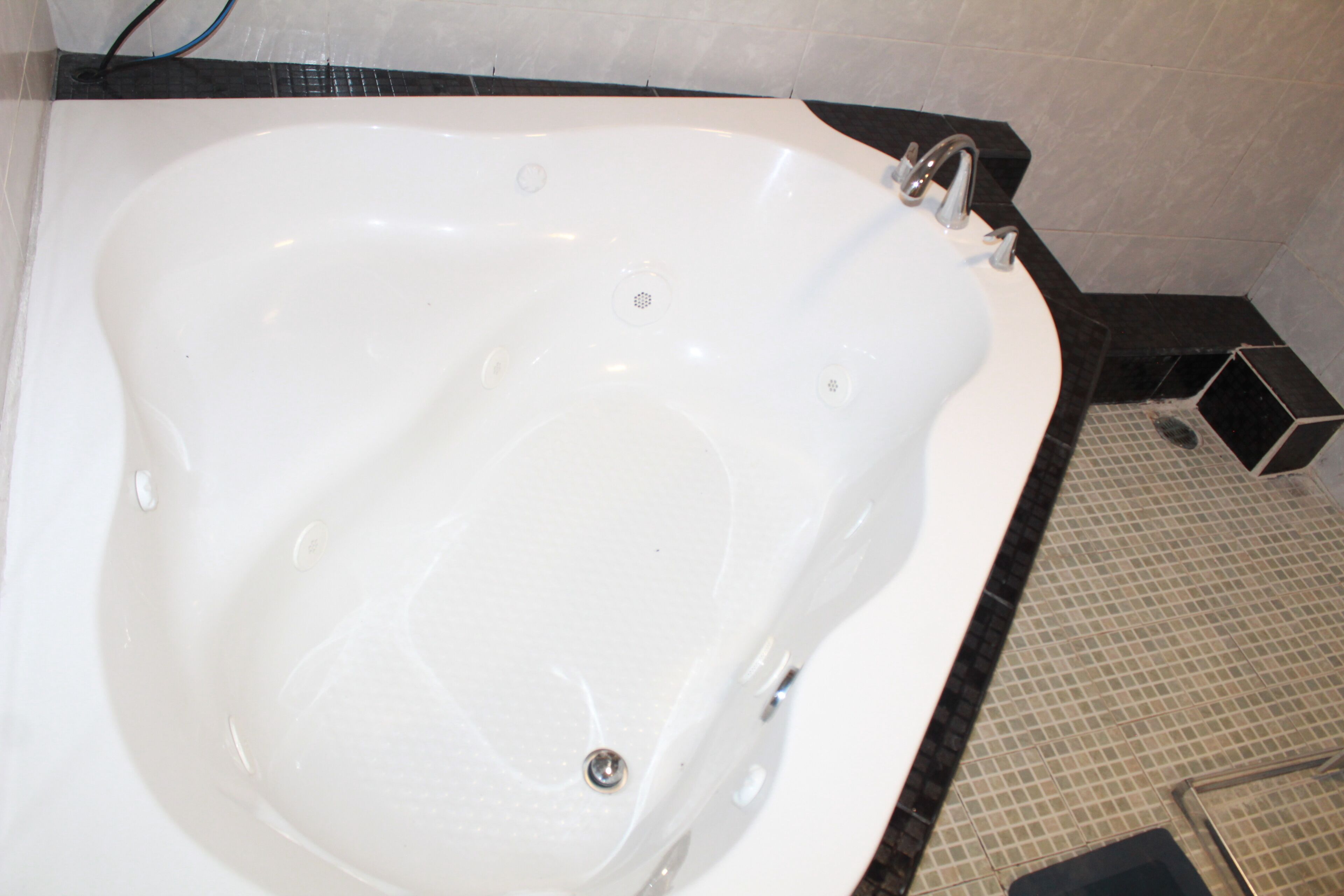 Una bañera blanca con una llave monocomando, suelo de baldosas y encimera negra.