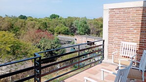 Un balcon donnant sur une zone boisée et un mur en briques.