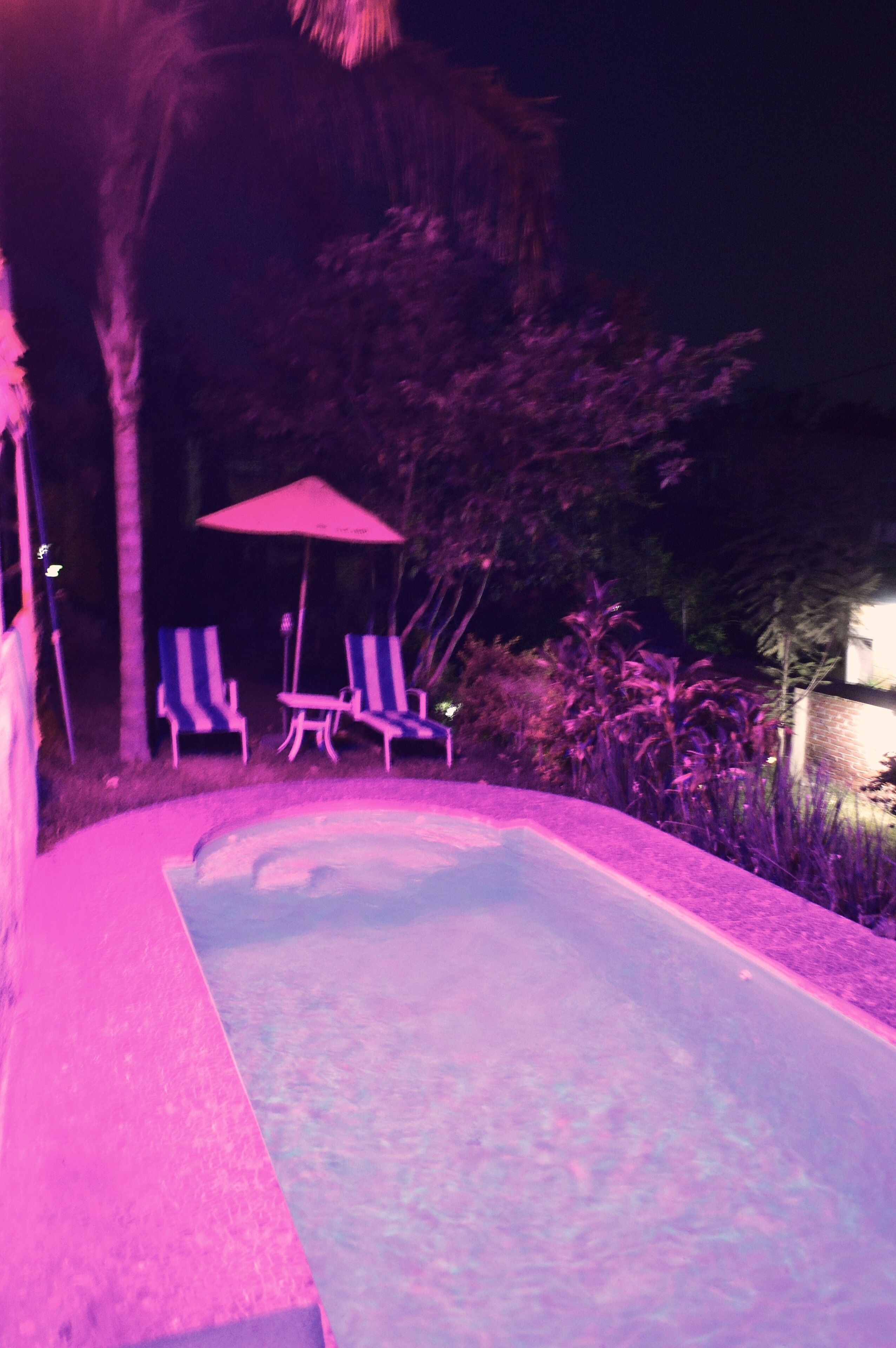 A swimming pool with lounge chairs and an umbrella.
