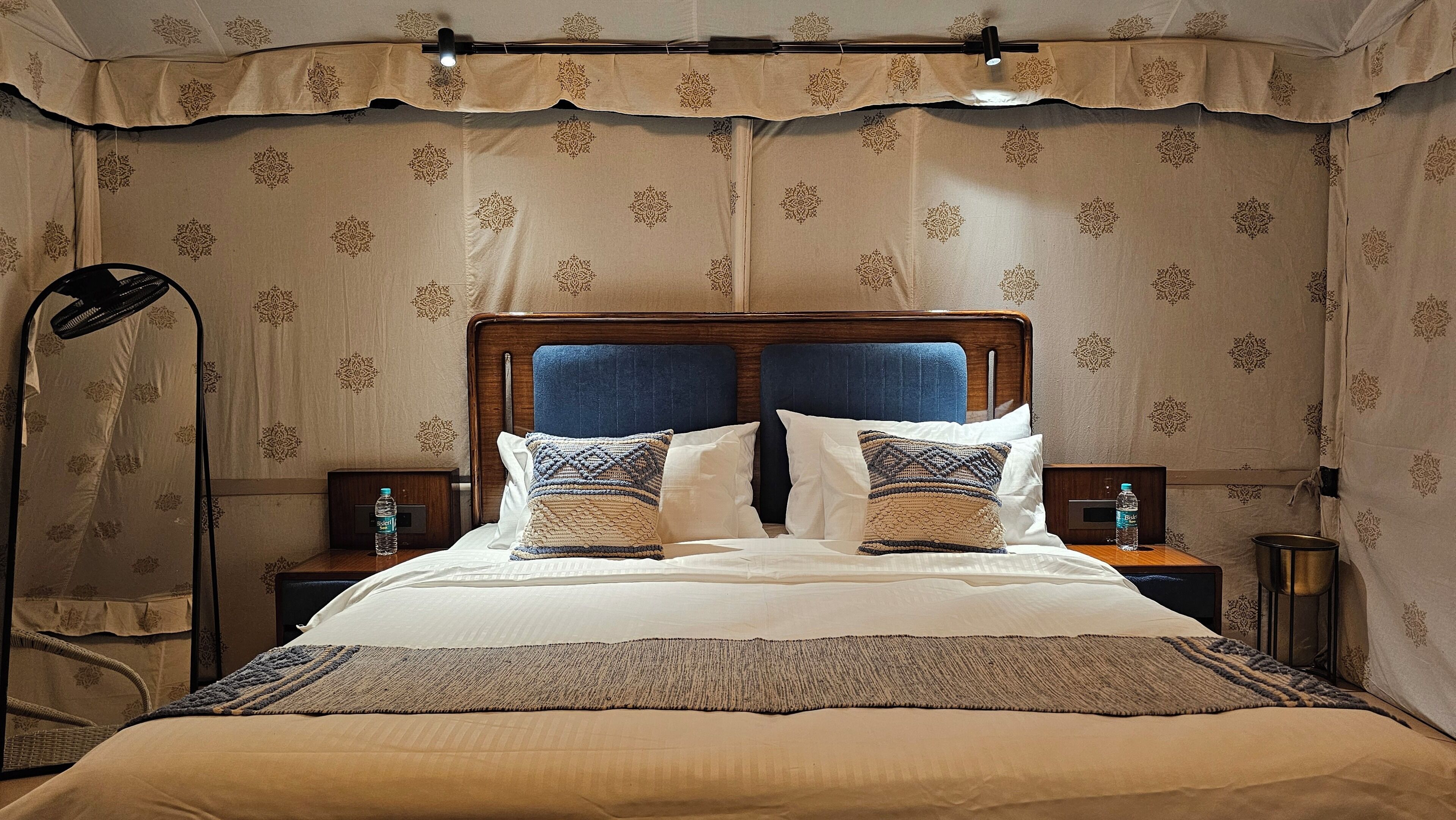 A hotel room with a large bed, two bedside tables, a floor lamp, and patterned wallpaper.