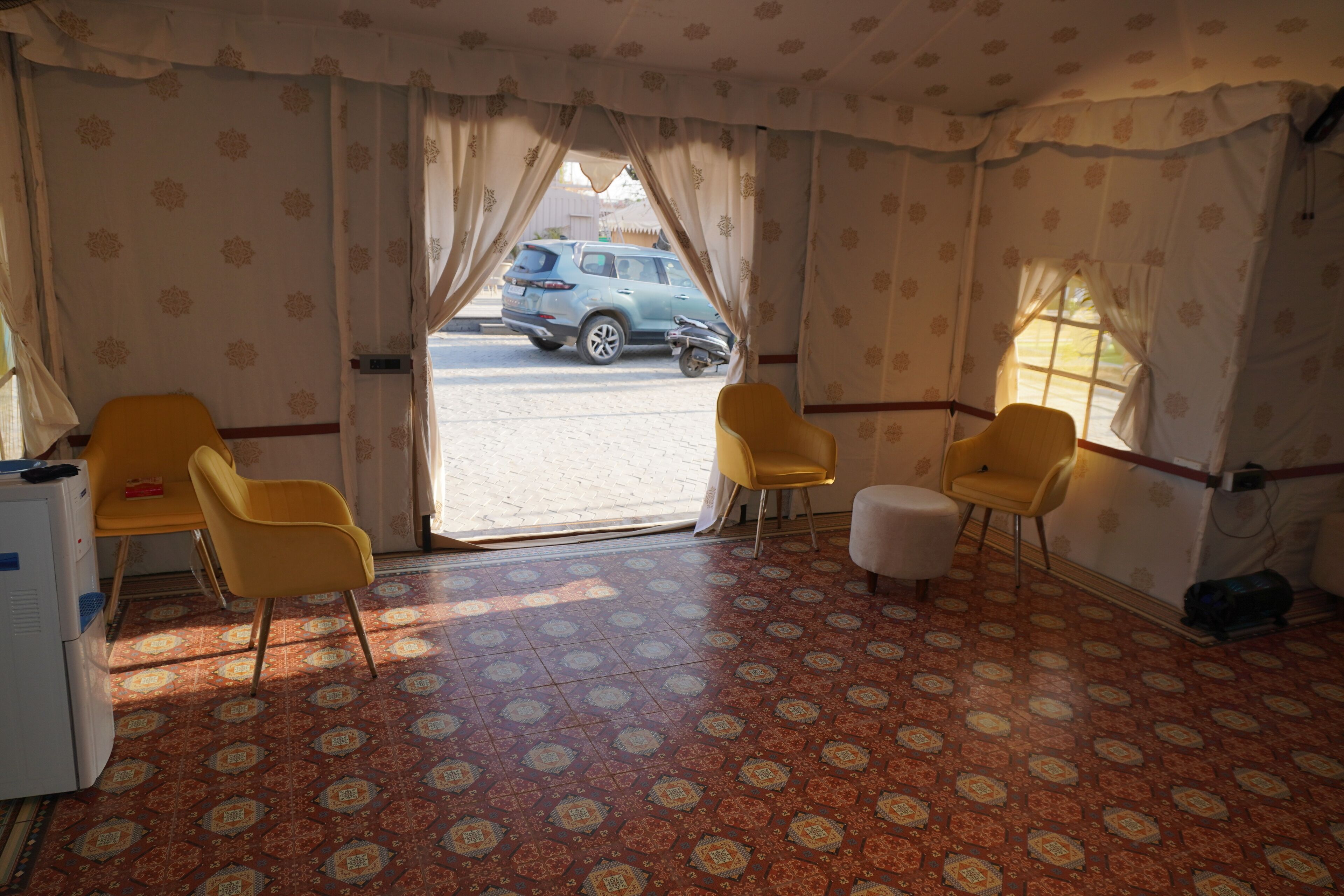 A room with patterned carpet, two yellow chairs, a small table, and a window with curtains.