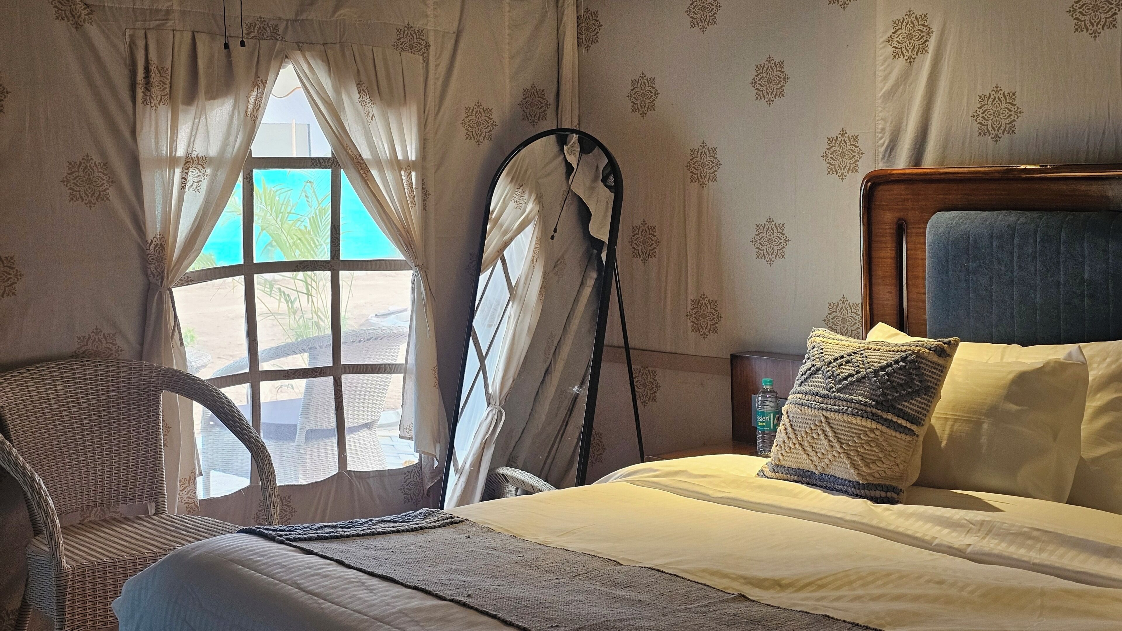 Un dormitorio con cama, una silla, un ventanal con cortinas y un papel tapiz con diseño.