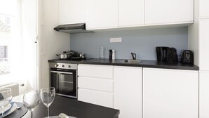 Eine moderne Küche mit weißen Schränken, einer schwarzen Arbeitsplatte und Edelstahlgeräten, darunter ein Backofen und eine Kaffeemaschine.