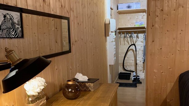 A wooden interior with a desk, a mirror, a framed picture, and a view into another room with a vacuum cleaner. - Comfortable Ski Stay in Mont-dore (Mont-Dore)