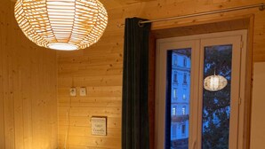 A wooden room with a bed, a nightstand with a lamp, a window with curtains, and a radiator. - Comfortable Ski Stay in Mont-dore (Mont-Dore)