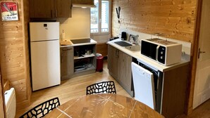 A compact kitchen with wooden walls, a refrigerator, a microwave, and a dining table with chairs. - Comfortable Ski Stay in Mont-dore (Mont-Dore)