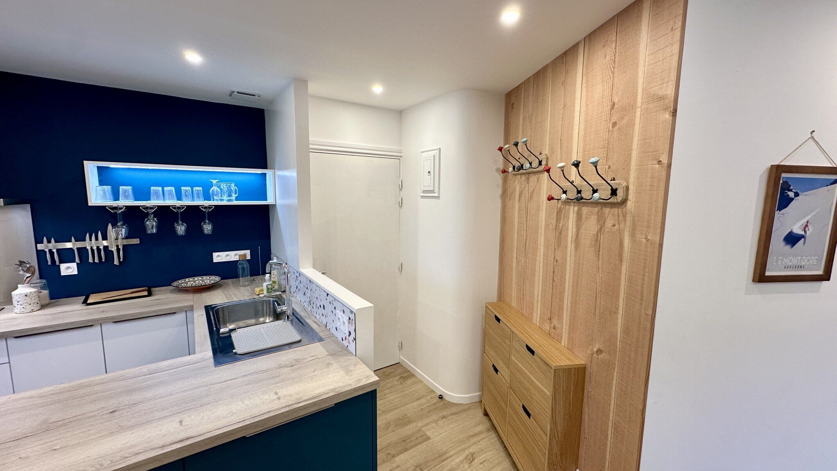 A modern kitchen with a blue backsplash, wooden cabinets, and a wooden wall-mounted rack.