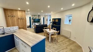 A compact kitchen with a wooden countertop, a built-in dishwasher, and a dining area with a table and chairs. - Modern Refuge Near the Village rim (Mont-Dore)