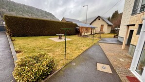 Un quartiere residenziale con un vialetto lastricato, un prato curato e un siepe. Si vedono case con stili architettonici diversi, tra cui una con tetto spiovente e un'altra con tetto piatto.