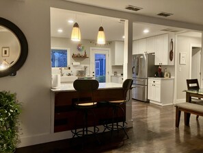 A modern kitchen with white cabinets, a stainless steel refrigerator, and pendant lighting.