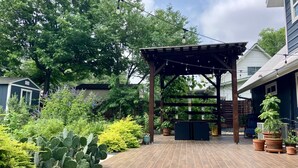 Ein überdachter Patio-Bereich mit einer Pergola, Kübelpflanzen und einem Backsteinboden.