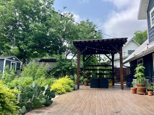 A covered patio area with a pergola, potted plants, and a brick floor.