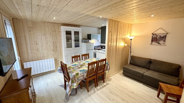 A cozy room with a dining table and chairs, a sofa, a TV, and a kitchen area. - Breezy Nook Near the ski Resort (Mont-Dore)