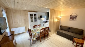 A cozy room with a dining table and chairs, a sofa, a TV, and a kitchen area. - Breezy Nook Near the ski Resort (Mont-Dore)