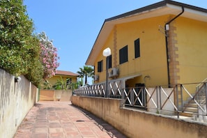 A yellow building with a staircase leading to a door, surrounded by a metal railing and a concrete wall. - Holiday Properties Sicilian Breeze2 (Lido di Noto, Italy)