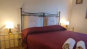 A neatly made bed with a red bedspread and two rolled towels on the side. - Holiday Properties Sicilian Breeze2 (Lido di Noto, Italy)