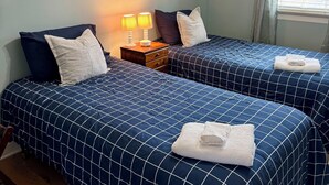 Une chambre d’hôtel avec deux lits, chacun recouvert d’une couvre-lit à motifs géométriques bleus, une table de chevet avec une lampe et des œuvres d’art abstraites accrochées aux murs.