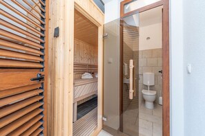 Puinen sauna, jossa on lasiovi, joka johtaa kylpyhuoneeseen, jossa on wc ja pesuallas.