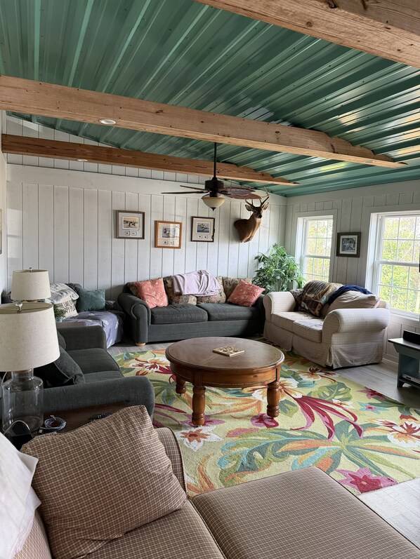 A cozy living room with a wooden ceiling, a mounted deer head, and a floral rug.