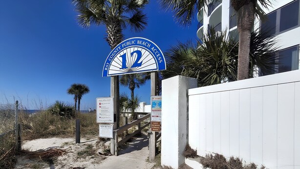 Un letrero de acceso a la playa con una palmera y un edificio al fondo.