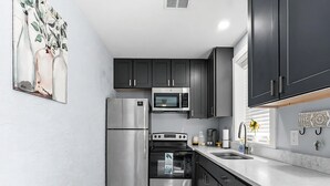 Una cocina moderna con armarios oscuros, electrodomésticos de acero inoxidable y encimera blanca.