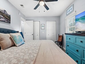 Ein Schlafzimmer mit Bett, Deckenventilator, Kommode und Fernseher an der Wand.