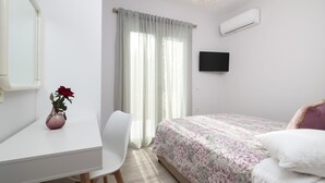 Un dormitorio con cama, escritorio, silla, un florero con flores, televisor y aire acondicionado.