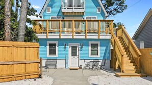 Una casa de dos pisos con fachada azul, un porche delantero y una escalera de madera que conduce a la entrada.