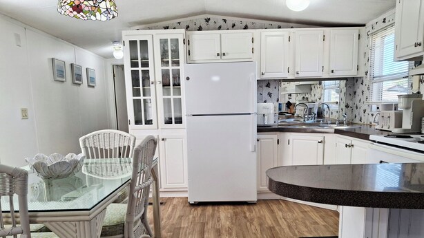 Cocina compacta con armarios blancos, un refrigerador blanco, una mesa de comedor con sillas de mimbre y una mesita redonda.