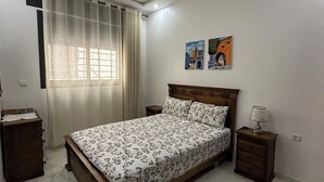 A bedroom with a bed, a nightstand, a dresser, a window with curtains, and two wall art pieces. - Enjoy staying in a calm apatment- near the beach with air conditioning and wifi (Martil)
