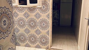 Ein Zimmer mit Wandfliesen mit Muster, einem Fenster und einer Tür zu einem Küchenbereich.