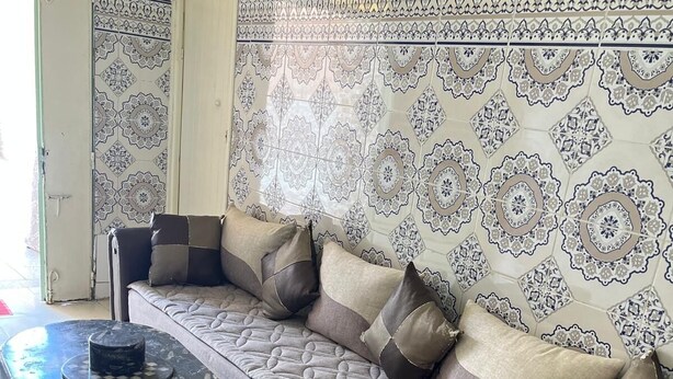 Ein modernes Wohnzimmer mit einer Couch, Hocker und Wandfliesen mit Muster.