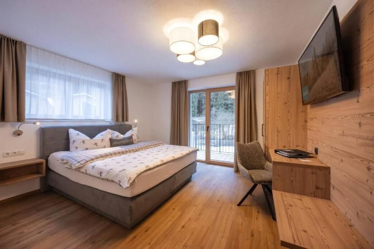 Een slaapkamer met een bed, nachtkastjes, een stoel, een televisie en een schuifglazen deur naar een balkon.