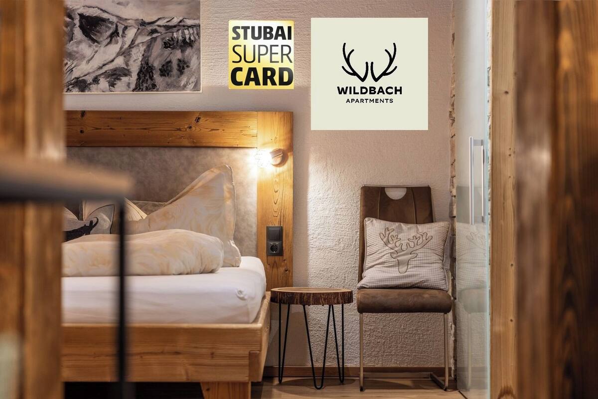 Een slaapkamer met een houten hoofdbord, een bed met witte beddengoed, een klein rond tafeltje en een stoel met een rendiermotief.