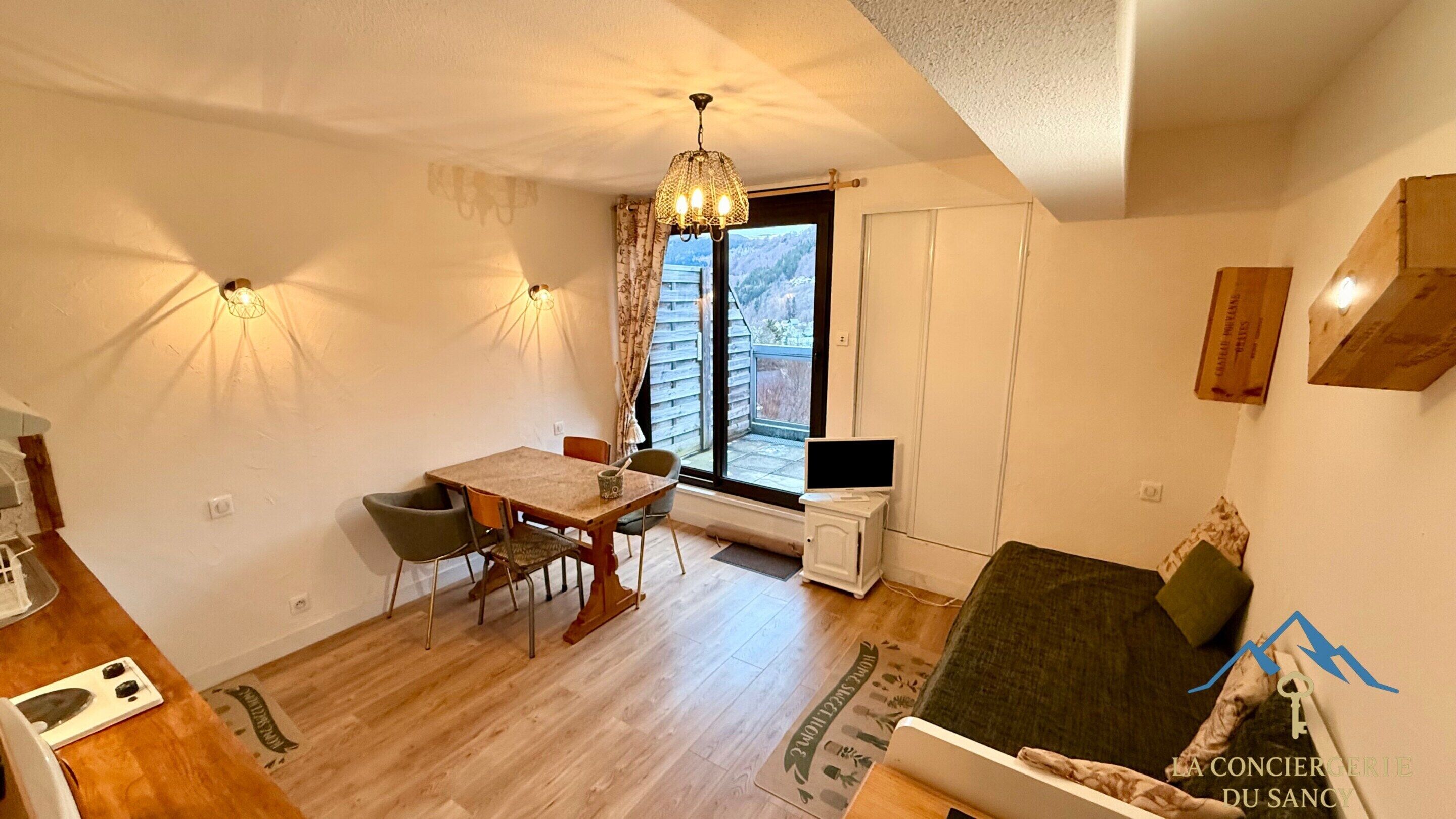 A compact living space with a dining area, a sofa, a TV, and a window with a view of the outdoors.
