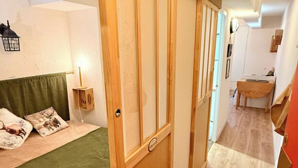 Una habitación con una cama, una puerta corredera de madera, una mesita y un banco.