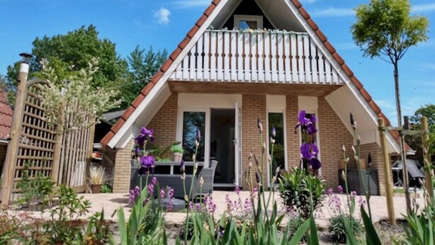 Een huis met twee verdiepingen, een balkon, een deur en een kleine tuin met paarse bloemen.