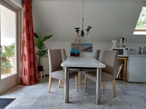 A dining area with a white table, four chairs, a chandelier, a potted plant, and a view of the outdoors. - Cozy Holiday Home in Burgerbrug (Burgerbrug)