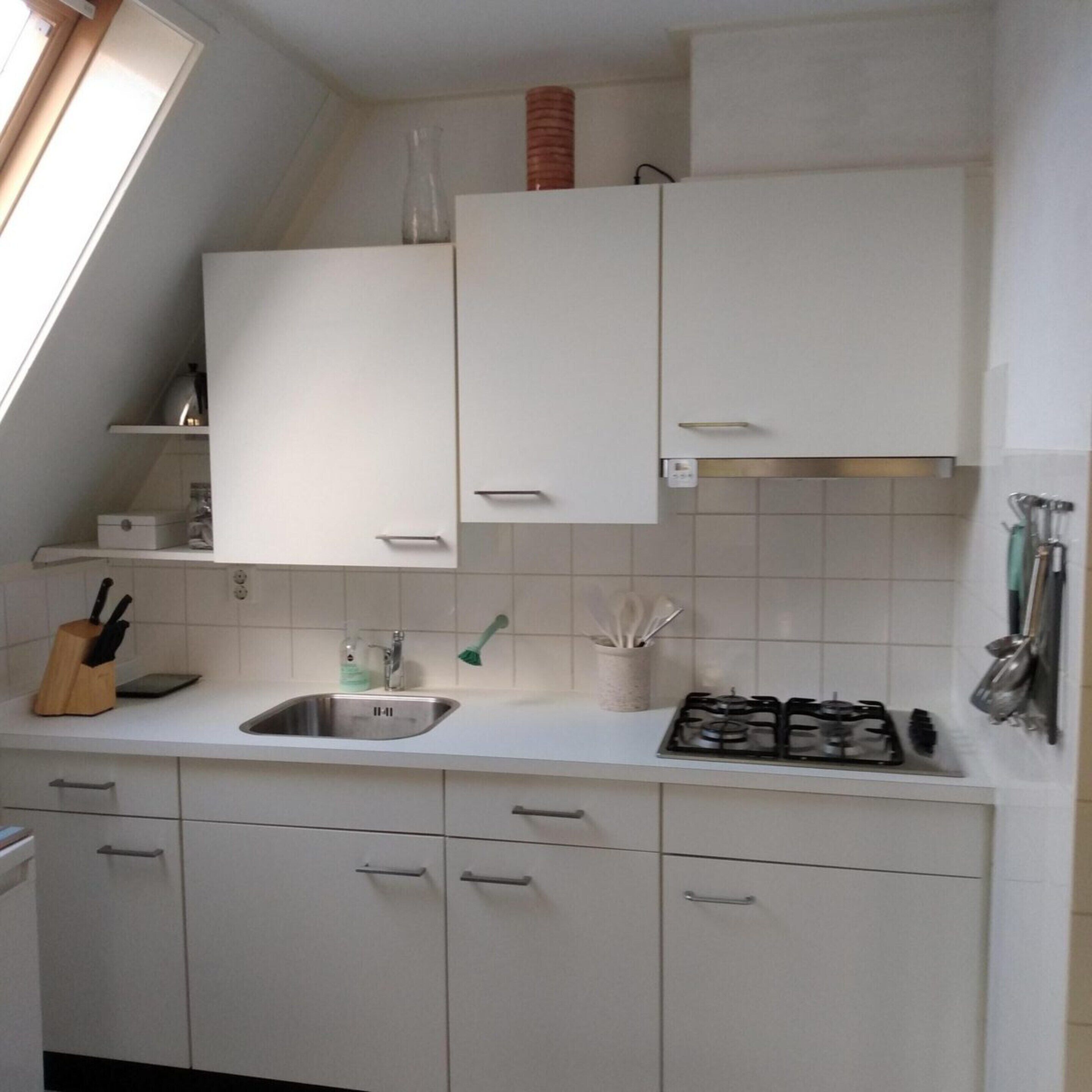Eine Küche mit weißen Schränken, einer Edelstahl-Spüle, einem Gasherd und einem Fenster über der Spüle.