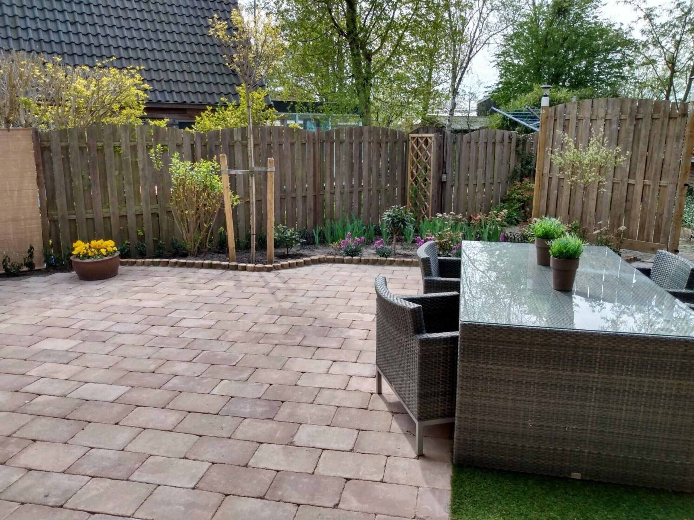 Uma área de pátio com piso de tijolos, móveis de vime e plantas em vasos.