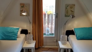 Een knus kamertje met twee bedden, een deur naar een balkon en twee bedlampjes.