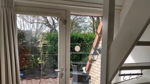 Uitzicht vanuit een kamer met een schuifdeur naar een patio met betegelde vloer, een kleintje tafel en een stoel.
