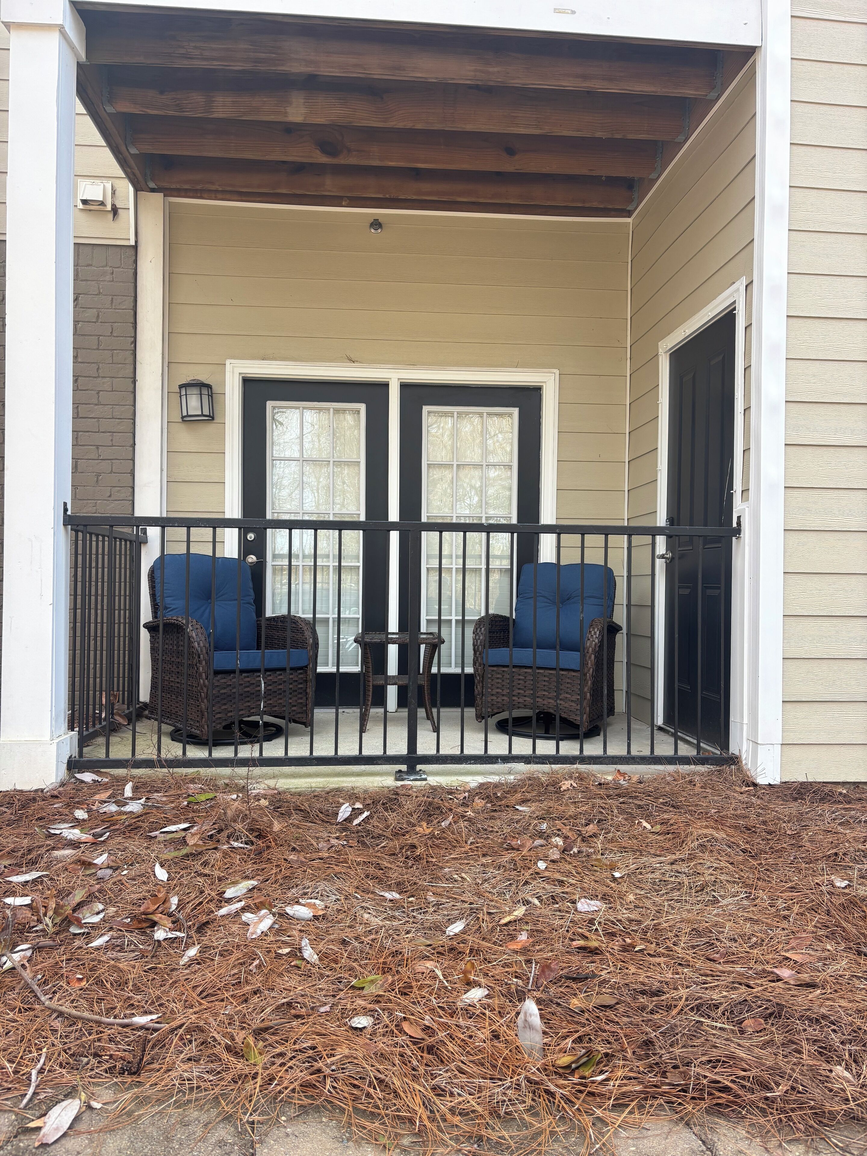 A porch with two wicker chairs and a small table, a double door, and a light fixture above the door.