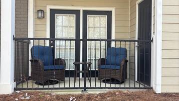 A porch with two wicker chairs and a small table, a double door, and a light fixture above the door.