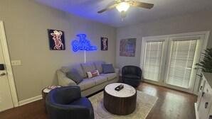 Ein Wohnzimmer mit Sofa, zwei Sesseln, einem Couchtisch, einem Deckenventilator und einem Neonzeichen.