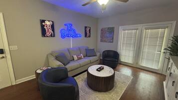 A living room with a sofa, two armchairs, a coffee table, a ceiling fan, and a neon sign.