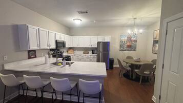 A modern kitchen with white cabinets, a central island with bar stools, a dining area with a round table and chairs, and a painting on the wall.