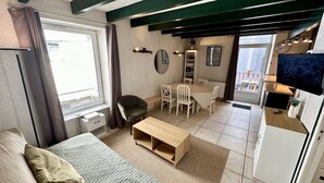 A compact room with a bed, a small desk, a dining table with chairs, a TV, and a balcony with a view. - T3 Montlosier Le Mont Dore 5/7 Pers (Mont-Dore)