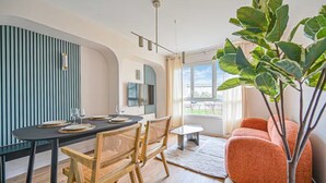 A modern living room with a dining area, featuring a black dining table, wooden chairs, a red sofa, and a large green plant. - PARIS - Adorable 3-room apartment with 2 bedrooms and 2 bathrooms (Bagnolet)