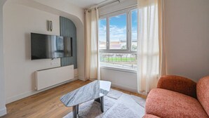 A modern living room with a flat-screen TV, a marble coffee table, a sofa, and a large window with curtains. - PARIS - Adorable 3-room apartment with 2 bedrooms and 2 bathrooms (Bagnolet)